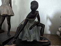 Close-up of seated ballerina statuette adjusting ballet shoe, showing costume detail and pose