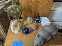 Wide shot of mixed lot items on wooden surface including candy dish, alabaster horse heads, glass globes, milk glass box, and wooden cat figurine.