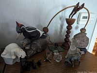 Mixed animal and insect figurines including a carved woodpecker on rock, polar bear, black dog trio, brass insect, glass animals, and a tall wooden balancing top with animal figure.