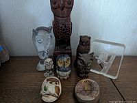 Overview photo showing nine owl-themed figurines and decorative items made of wood, glass, or stone, arranged on a wooden surface.