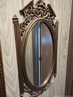 Oval wall mirror with elaborate carved floral and scroll motifs in gold/bronze finish.