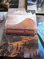 Photo of the book 'Unfinished Tales of Númenor and Middle-earth' showing a torn dust cover with characters depicted in the foreground and mountains in the background.