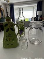 All four items visible on the table in natural light showing olive oil bottle, grapevine decorated bottle, spice container and glass jar.