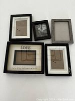 Top-down view of 5 assorted picture frames of various sizes and colors on white surface
