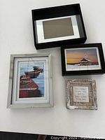 Four assorted picture frames laid out with two showing boat prints, one with shed print, one small frame with text and one empty.