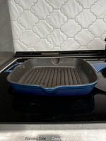 Side view of blue cast iron grill pan showing ribbed cooking surface and spout for pouring.