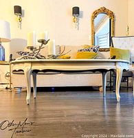 Front view of white painted wooden coffee table with curved legs and scalloped apron in a living room setting.
