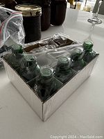 Six green glass drop dispenser bottles arranged in an aluminum tray, viewed from above.