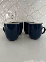 Four blue ceramic mugs grouped together on a white countertop against a light tile backsplash.