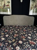 Frontal view of queen size beige upholstered headboard attached to a bed with floral bedspread, showing overall condition and missing one button.