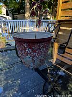Photo showing a hand painted plastic pot with a house plant inside on an outdoor glass table.