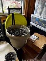 Large beige plastic planter containing a tangled bundle of outdoor string lights with clear bulbs and some cords.