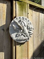 Front view of the round white ceramic solar clock painted with chalk paint showing butterfly and leaf relief design, mounted on wooden fence.
