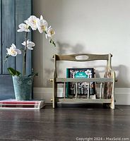 Front view of vintage hand-painted wooden magazine basket with greenish-gold finish and decorative decoupage sides. Basket contains some magazines but they are not included with the lot.