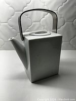 Front side view of the white ceramic teapot with square design, metal handle, and spout.