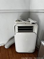 Front view of the portable window air conditioning unit showing white front panel with vent and controls and white window installation parts placed on top.