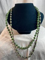 Two vintage stone bead necklaces shown on display bust. One necklace is green bead, the other is multi-tone green and reddish beads.