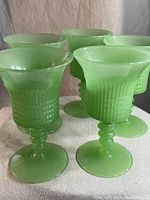 Five translucent jadeite green wine glasses with textured grid pattern and unique stems.