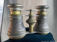 Front view of the silver etched Victorian opera glasses showing detailed floral and geometric patterning on metal barrels and central focusing mechanism.