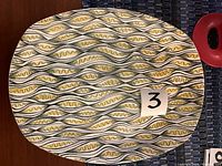 Top view of oval platter with abstract wavy geometric pattern in yellow, green and black over white.