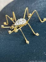 Close-up side angle of gold-tone spider brooch showing clear stones on body and feet, with onyx eyes.