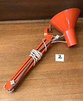 Orange mid-century architect-style adjustable arm task lamp with clamp and cone-shaped shade, with white adjustment knobs and visible cord.