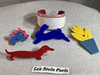 Photo showing all five jewelry pieces including four brooches and one bracelet, laid out on fabric, with a Lea Stein Paris label visible.