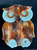 Front view of vintage owl-shaped Lea Stein brooch featuring marbled brown body, blue eyes, and orange rims.