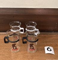 Four Bodum Monkey glass coffee mugs arranged on wooden surface, two with black handles in front and two with white handles behind, showing printed monkey design and Bodum logo.