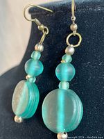 Close-up front view of one earring showing frosted aqua blue round beads and disc bead with gold-toned metal hook and spacer beads