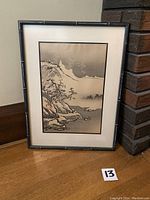 Frontal image of the vintage Asian watercolour painting in black textured bamboo-like frame and white matting, showing mountains, trees and water landscape detail.