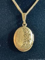 Front view of oval locket with floral etching and attached chain