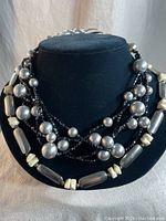 Front view of the multi-strand vintage necklace on a black bust, showing large silver beads, cream beads, and black faceted strands.