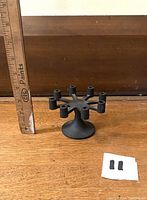 Front and side views of the black cast iron 8-arm candelabra with round base on wooden surface with ruler for scale and two small black parts placed beside it