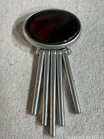 Front view of vintage brooch showing large oval amber cabochon in silver-tone mounting with five vertical rod dangles.
