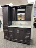 Full view of dark wood vanity ensemble with linen tower on left, base cabinet and countertop with sink, upper mirror cabinet and integrated lights