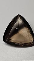 Trillion cut smokey quartz gemstone showing triangular faceted shape and transparency with one small visible inclusion.