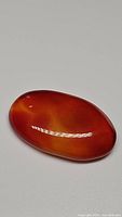Bright orange translucent oval cabochon carnelian gemstone shown on plain white background with visible reflections.