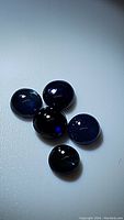 Five dark blue natural sapphire gemstones with round cabochon cut, showing polish and inclusions under lighting.