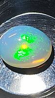 Close-up image showing oval cabochon natural untreated Ethiopian opal with strong green and yellow play of colors on a dark scratched metal surface.