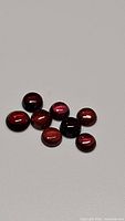 Photo showing 9 round cabochon garnet gemstones with variations of red, pink, and orange colors on a white surface.