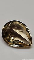 Close-up photo of the front side of a pear-shaped golden citrine gemstone with visible facets and good transparency.
