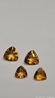 Four natural golden citrine gemstones in trillion cut displayed on a neutral background, showing the shapes and color.