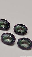 Four oval cut Mystic Topaz gemstones showing strong purple and rainbow color flashes from different angles.