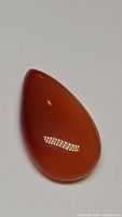 Front view of pear-shaped polished carnelian cabochon with reflective highlights showing smooth surface and rich reddish-orange color.