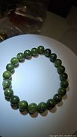 Close-up photo of green natural jade bead stretchy bracelet arranged circularly on a white surface with visible natural stone patterns and glossy finish.