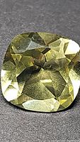 Close-up image of a yellow cushion cut lemon citrine gemstone showing faceted surface and natural inclusions.