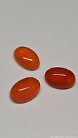 Three natural mandarin orange carnelian oval cabochon gemstones with bright, deep orange color and polished surfaces.