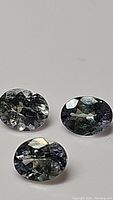 Three oval cut multicolored natural tanzanite gemstones on a plain background showing facets and color play.