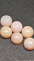 Six natural pink opal cabochons displayed on dark background, polished round and smooth, soft pink to peach tones visible, similar set in two photos.